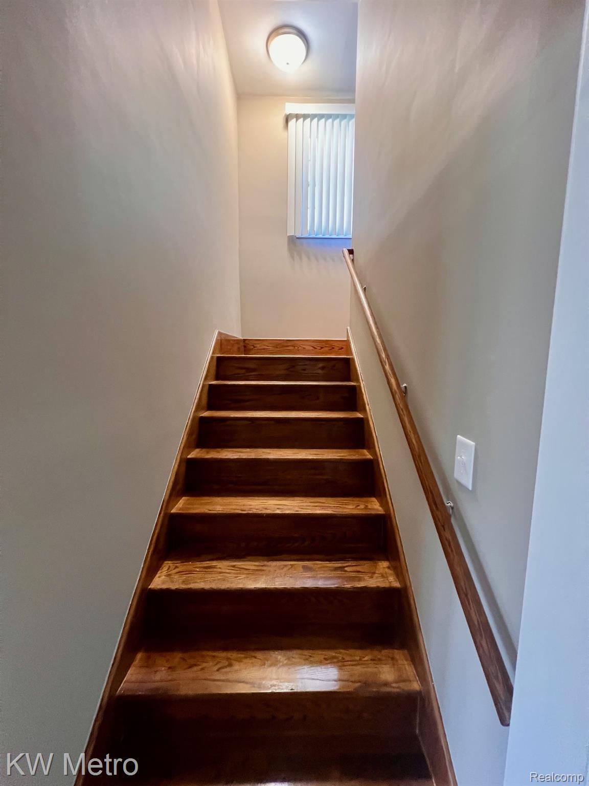 939 Webb Street Detroit, MI 48202 - Photo 7 of 19 Hardwood staircase featuring a natural wood handrail, neutral wall paint, and a wall-mounted light fixture