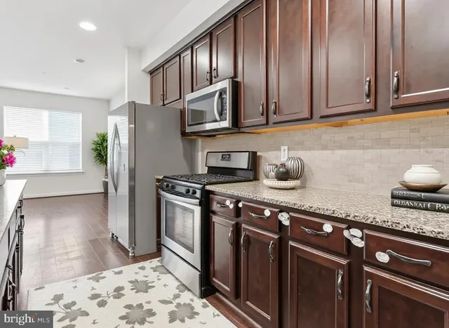 a kitchen with stainless steel appliances granite countertop a refrigerator a stove and a sink with wooden cabinets