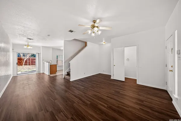 a view of an empty room with wooden floor and a ceiling fan