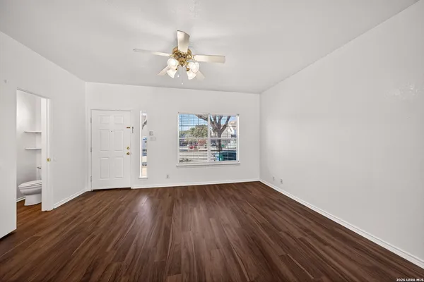 an empty room with wooden floor chandelier fan and windows