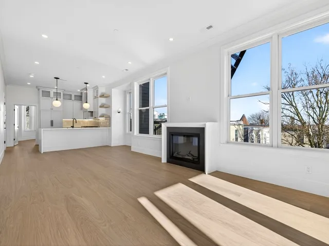 a living room with stainless steel appliances furniture a fireplace and a kitchen view