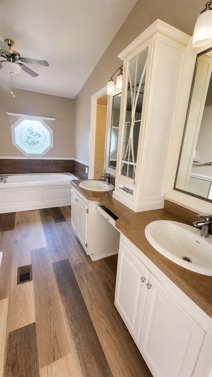 9455 Tranquil Acres Road Fort Worth, TX 76179 - Photo 15 of 20 Bathroom featuring wood-finish flooring, a white soaking tub beneath an octagon-shaped window, and a dual vanity with white cabinetry