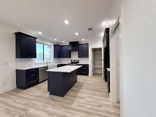 a kitchen with stainless steel appliances granite countertop wooden cabinets a sink a stove a refrigerator and island with wooden floor