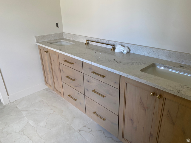 4676 West 75 North, Unit 401 West Point, UT 84015 - Photo 16 of 17 Double vanity featuring light wood cabinetry, gold-tone hardware, and light-toned stone countertops with integrated sinks