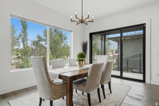 653 East Vandalay Lane Draper, UT 84020 - Photo 16 of 61 Dining area featuring wood-finish flooring, a contemporary chandelier, expansive windows, and glass sliding doors opening to an exterior deck with metal railings