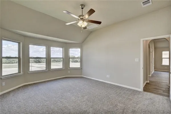 an empty room with chandelier fan and windows