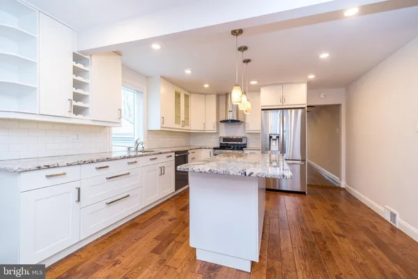 a kitchen with stainless steel appliances granite countertop a refrigerator a sink dishwasher a stove and white cabinets with wooden floor