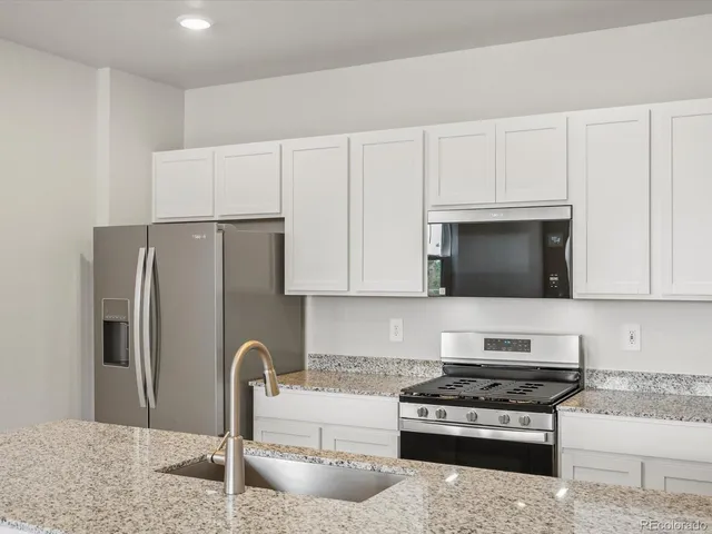 a kitchen with stainless steel appliances granite countertop a refrigerator stove and white cabinets