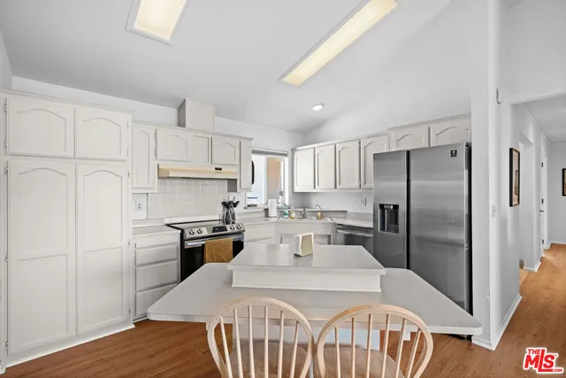 a kitchen with kitchen island a refrigerator a stove a sink dishwasher a dining table and chairs with wooden floor