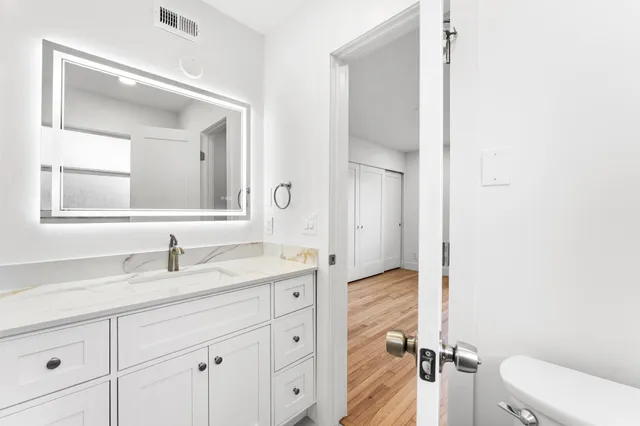 a bathroom with a granite countertop sink vanity mirror and toilet