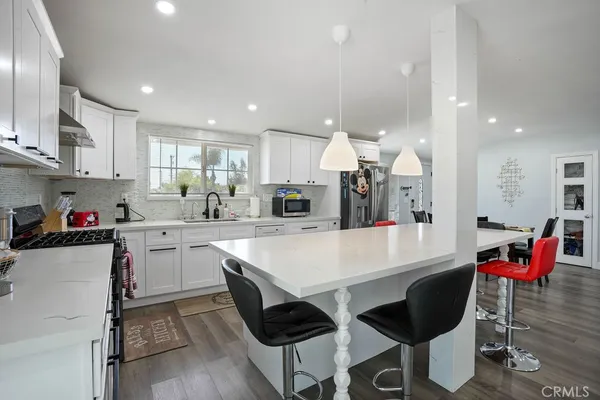 a large white kitchen with stainless steel appliances kitchen island granite countertop a table chairs sink and cabinets