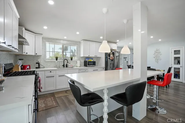 a large white kitchen with stainless steel appliances kitchen island granite countertop a table chairs sink and cabinets