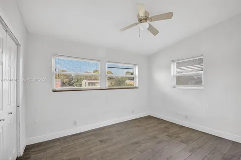 a view of an empty room with wooden floor and a ceiling fan