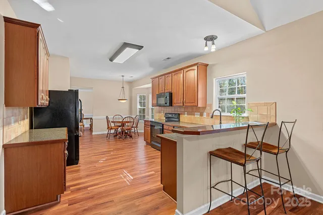 a kitchen with stainless steel appliances granite countertop a stove top oven a refrigerator a dining table and chairs with wooden floor