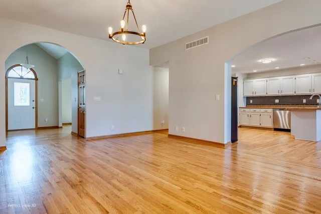 a view of empty room with wooden floor and kitchen