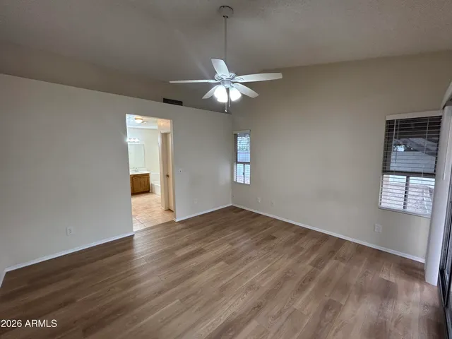 an empty room with wooden floor chandelier fan and windows