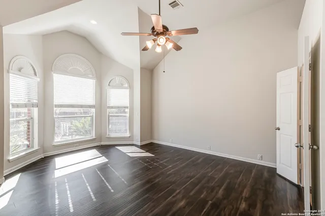 an empty room with wooden floor fan and windows