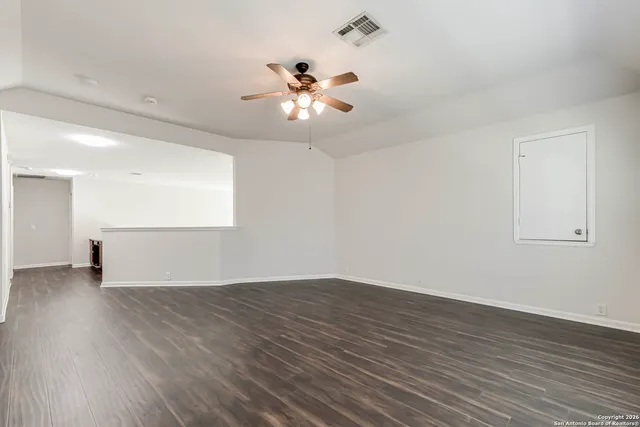 a view of an empty room with wooden floor and a ceiling fan
