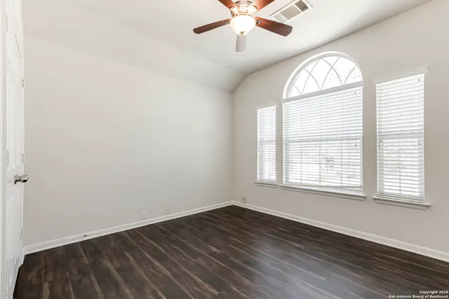 an empty room with wooden floor chandelier fan and windows