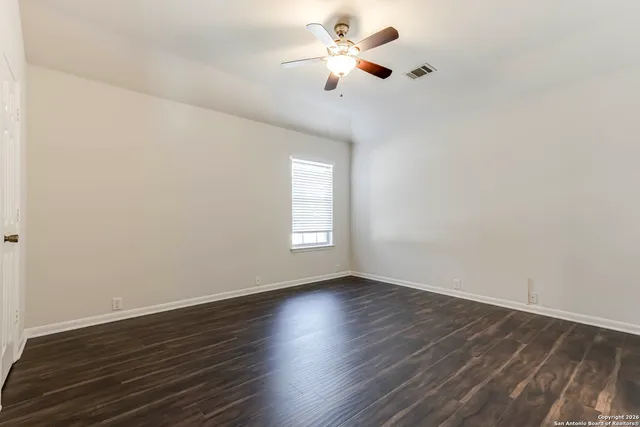 a view of an empty room with wooden floor and a ceiling fan