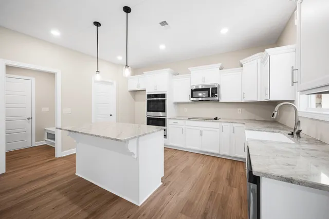 a kitchen with stainless steel appliances granite countertop a sink a stove a refrigerator and white cabinets with wooden floor