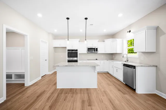 a kitchen with stainless steel appliances a refrigerator a sink dishwasher a stove and white cabinets with wooden floor