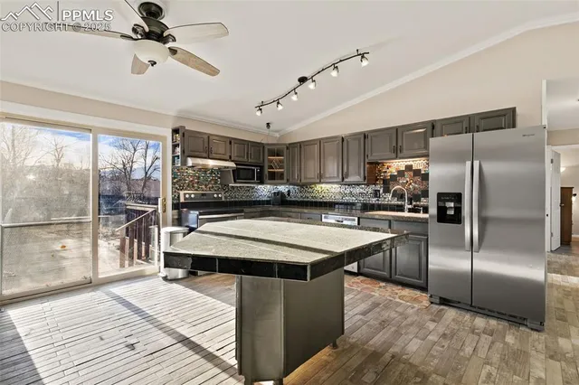 a kitchen with stainless steel appliances kitchen island granite countertop a refrigerator a sink dishwasher a stove and a refrigerator with wooden floor