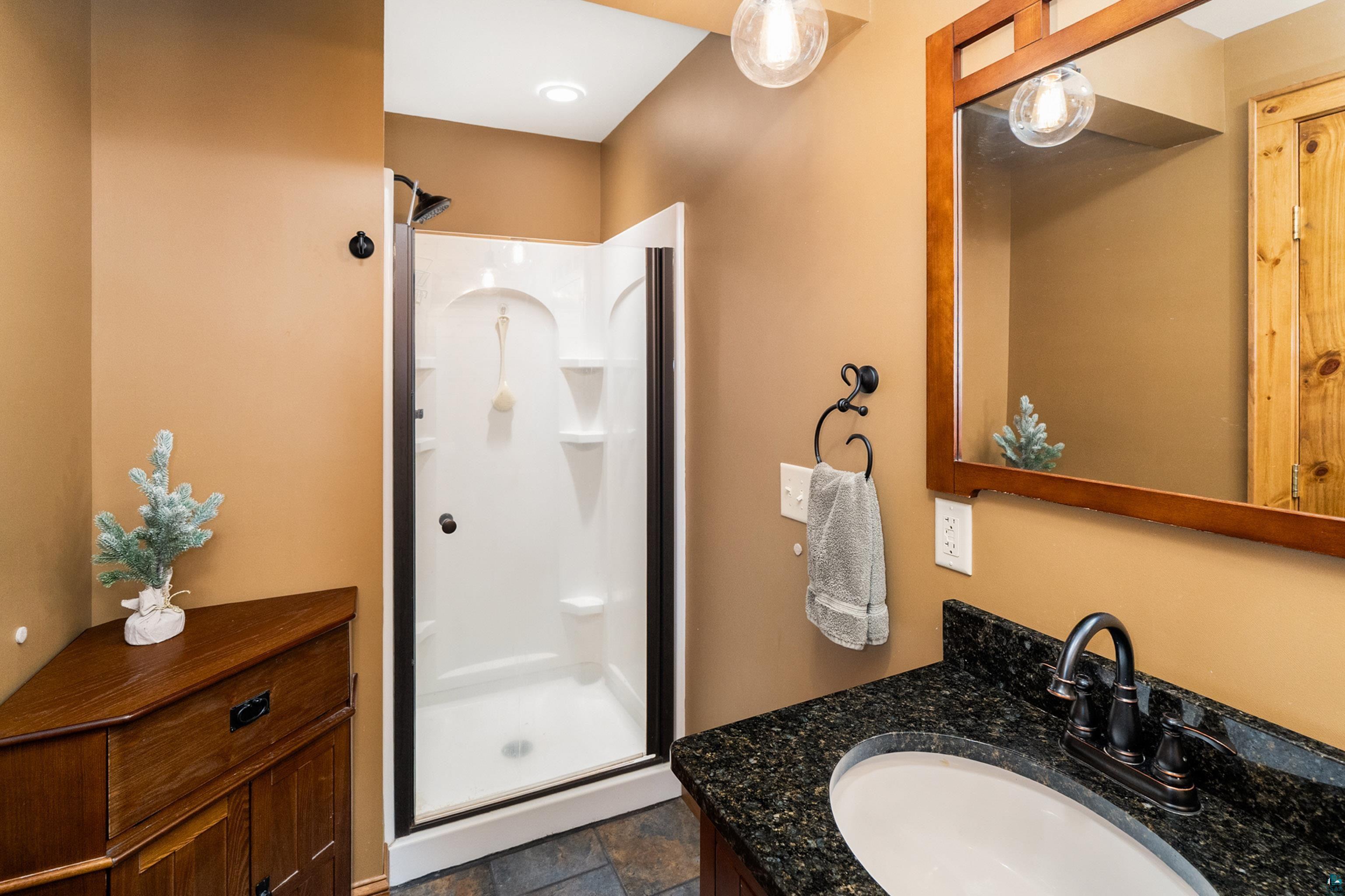 75 East Stark Road Esko, MN 55733 - Photo 44 of 87 Bathroom featuring a stand-up shower with dark bronze framing, dark granite countertop with an undermount sink, and a wood-framed mirror