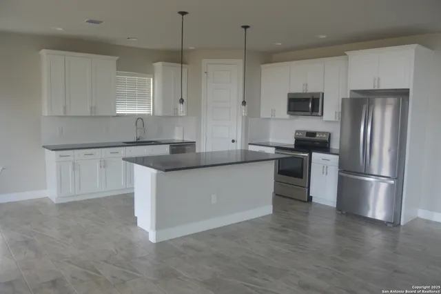 a kitchen with stainless steel appliances granite countertop a refrigerator a sink a stove and white cabinets