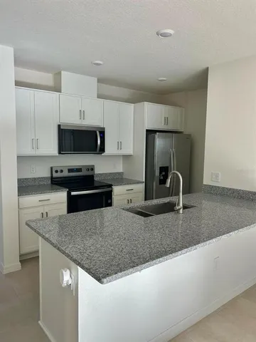 a kitchen with granite countertop a sink a stove a microwave a refrigerator and white cabinets