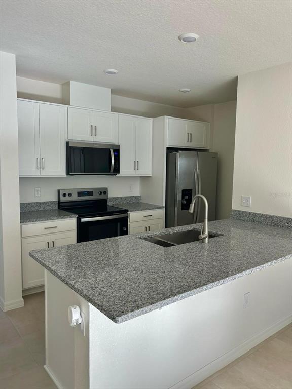 2787 Raindrop Run Street Clermont, FL 34714 - Photo 4 of 18 a kitchen with granite countertop a sink a stove a microwave a refrigerator and white cabinets