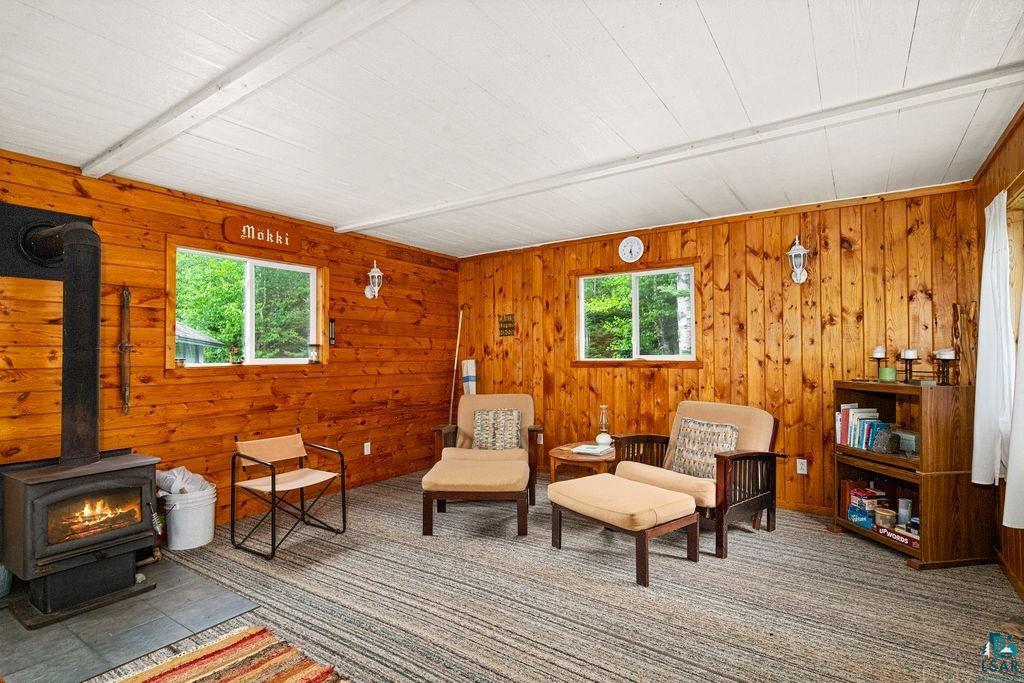 1268 Tom Lake Road Hovland, MN 55606 - Photo 3 of 56 Room featuring natural wood paneling, a wood-burning stove with a visible flame, and a white planked ceiling