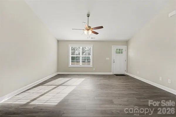 an empty room with wooden floor ceiling fan and windows
