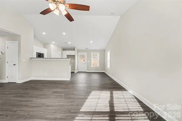 a view of an empty room with wooden floor and a ceiling fan