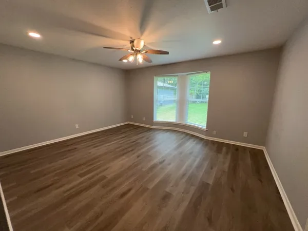 an empty room with wooden floor chandelier fan and windows