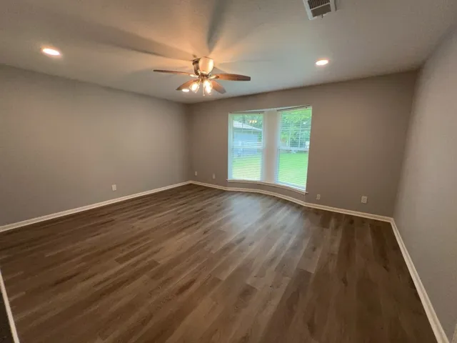 an empty room with wooden floor chandelier fan and windows