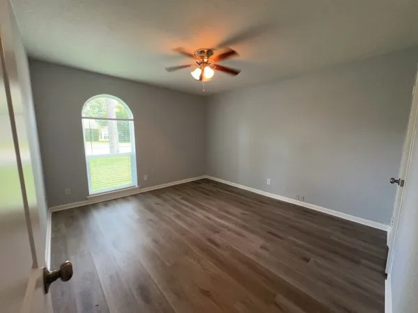an empty room with wooden floor fan and window