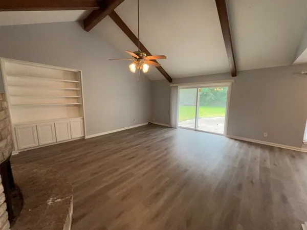 a view of an empty room with wooden floor and fan