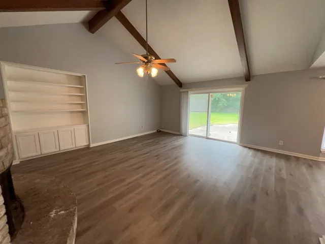 a view of an empty room with wooden floor and fan