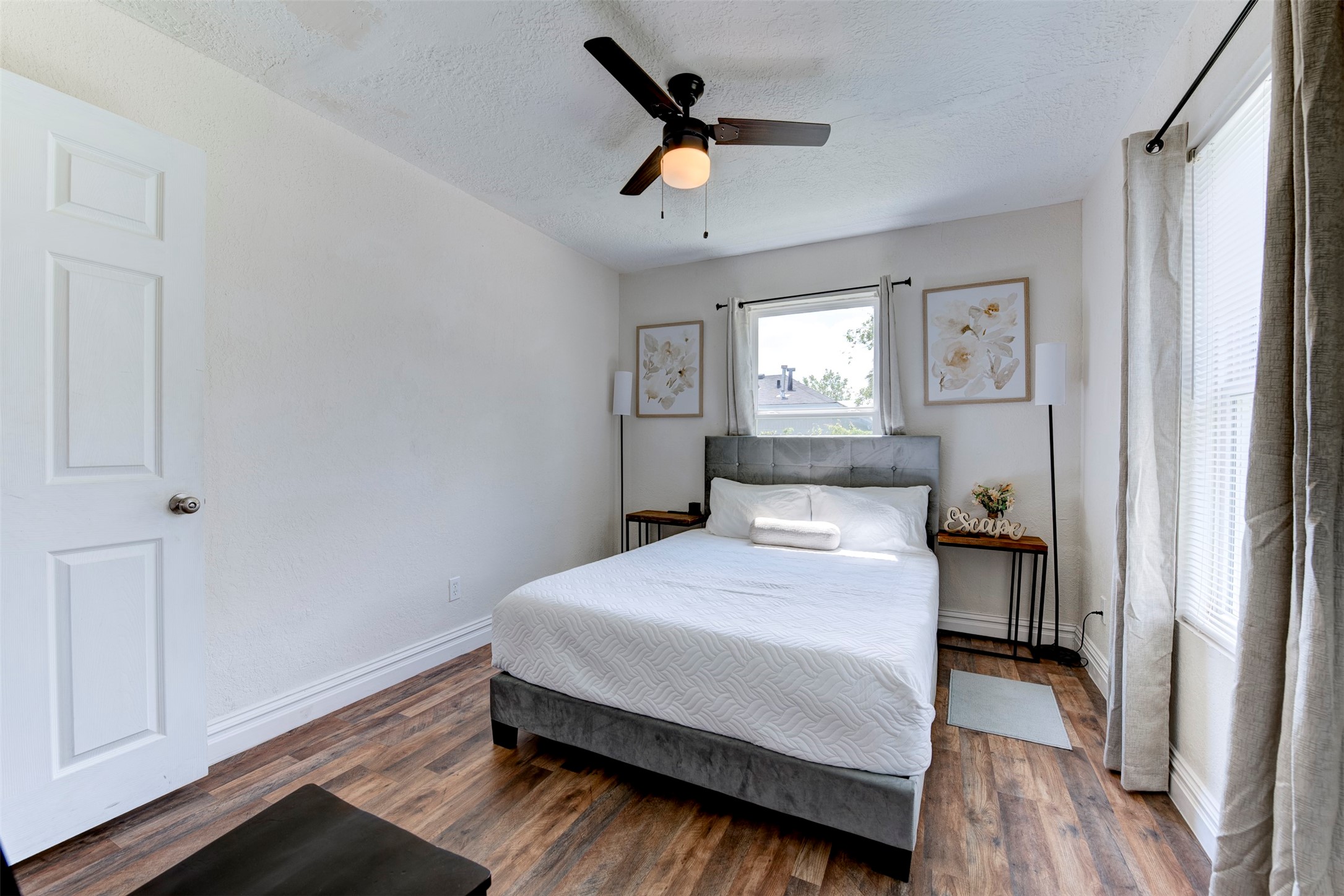 1121 Panama Street Houston, TX 77009 - Photo 25 of 35 Second bedroom with dark wood-look LVP flooring, ceiling fan with light kit, oversized window with grommet curtains on black rod, and six-panel interior door.