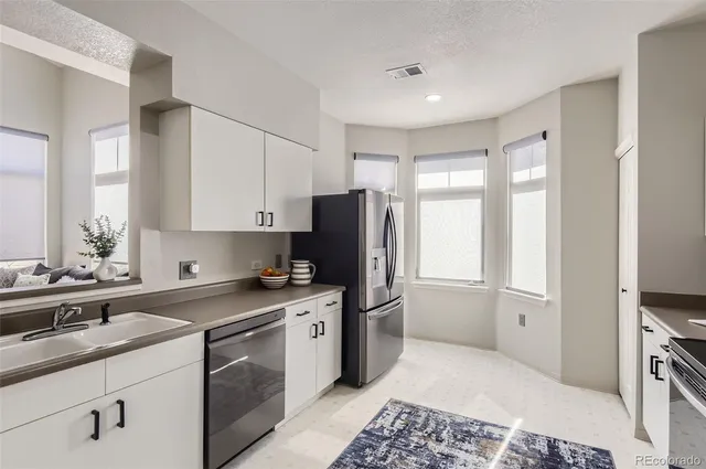 a kitchen with stainless steel appliances granite countertop a refrigerator stove a sink and white cabinets