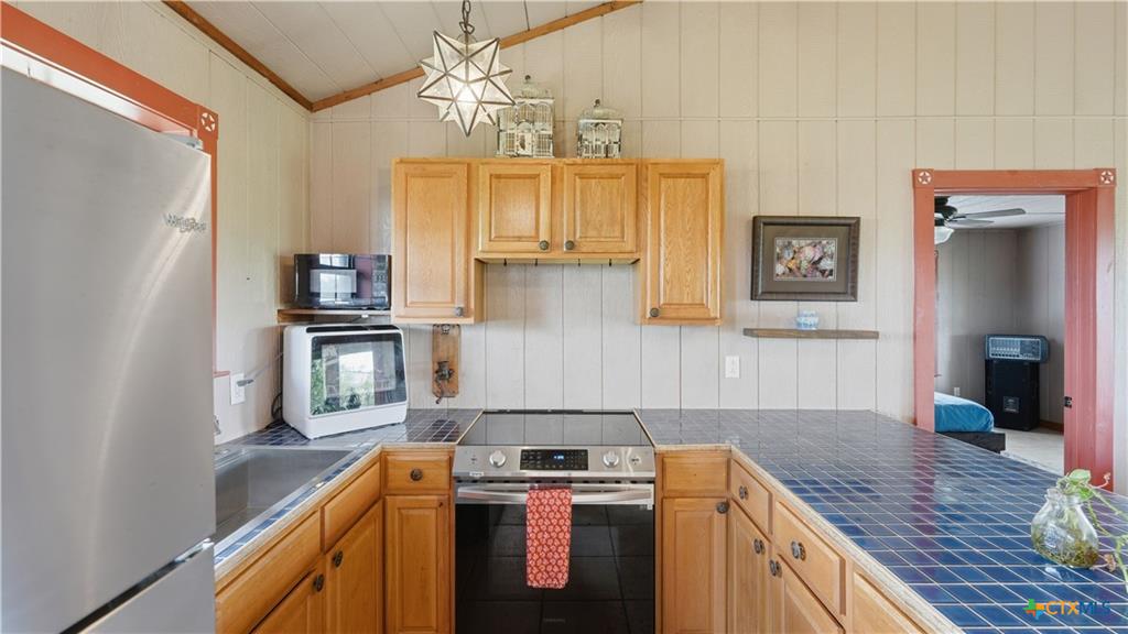 127 Offer Llano, TX 78643 - Photo 6 of 40 Kitchen featuring wood cabinetry, stainless steel appliances, blue tile countertops, and a built-in electric range