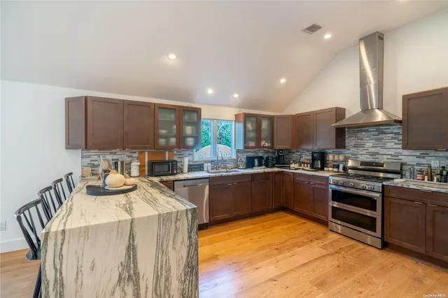 a kitchen with stainless steel appliances granite countertop a stove top oven a sink a dining table and chairs with wooden floor