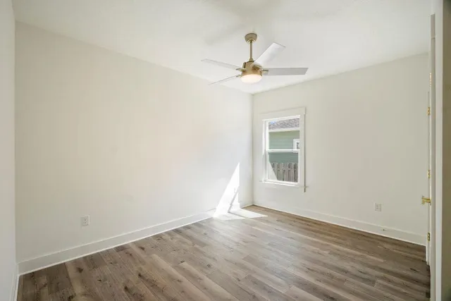 an empty room with wooden floor fan and windows