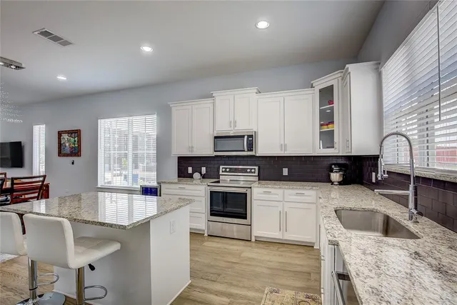 a kitchen with stainless steel appliances granite countertop a sink dishwasher a stove top oven a refrigerator with island and chairs