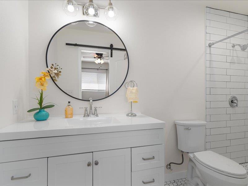 1312 Hyman Lane Austin, TX 78742 - Photo 23 of 36 Bathroom featuring a white vanity with silver hardware, a circular mirror, and a shower with white subway tiles