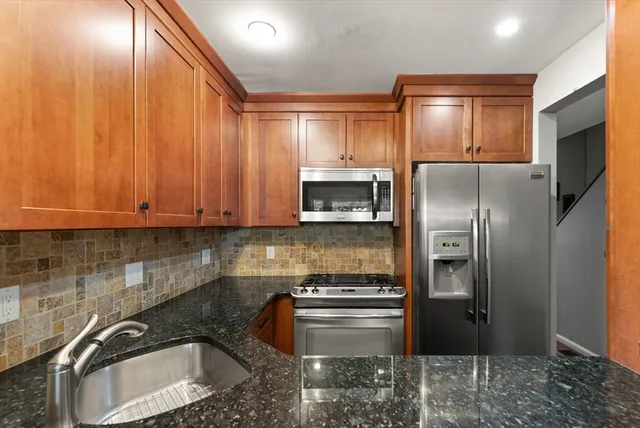 a kitchen with stainless steel appliances granite countertop a refrigerator a stove and a sink with wooden cabinets