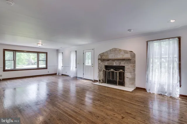 an empty room with wooden floor fireplace and windows