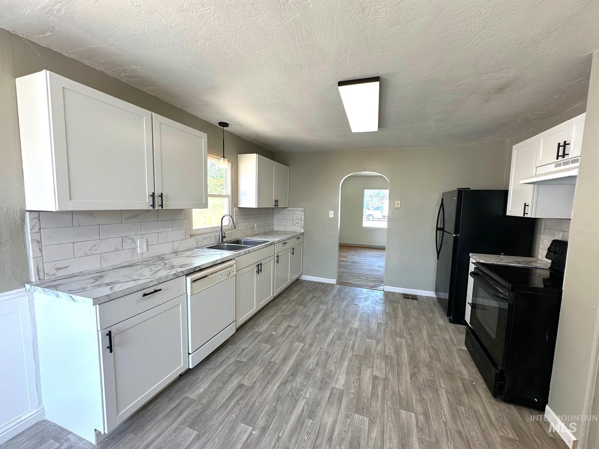 264 Southwest 10th Avenue Ontario, OR 97914 - Photo 5 of 26 Kitchen with arched walkways, black electric range oven, decorative backsplash, light wood-style floors, and a textured ceiling