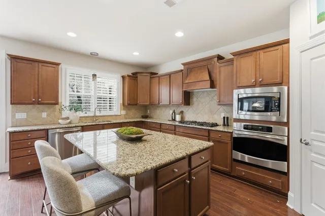 a kitchen with stainless steel appliances granite countertop a stove top oven a sink dishwasher a dining table and chairs with wooden floor